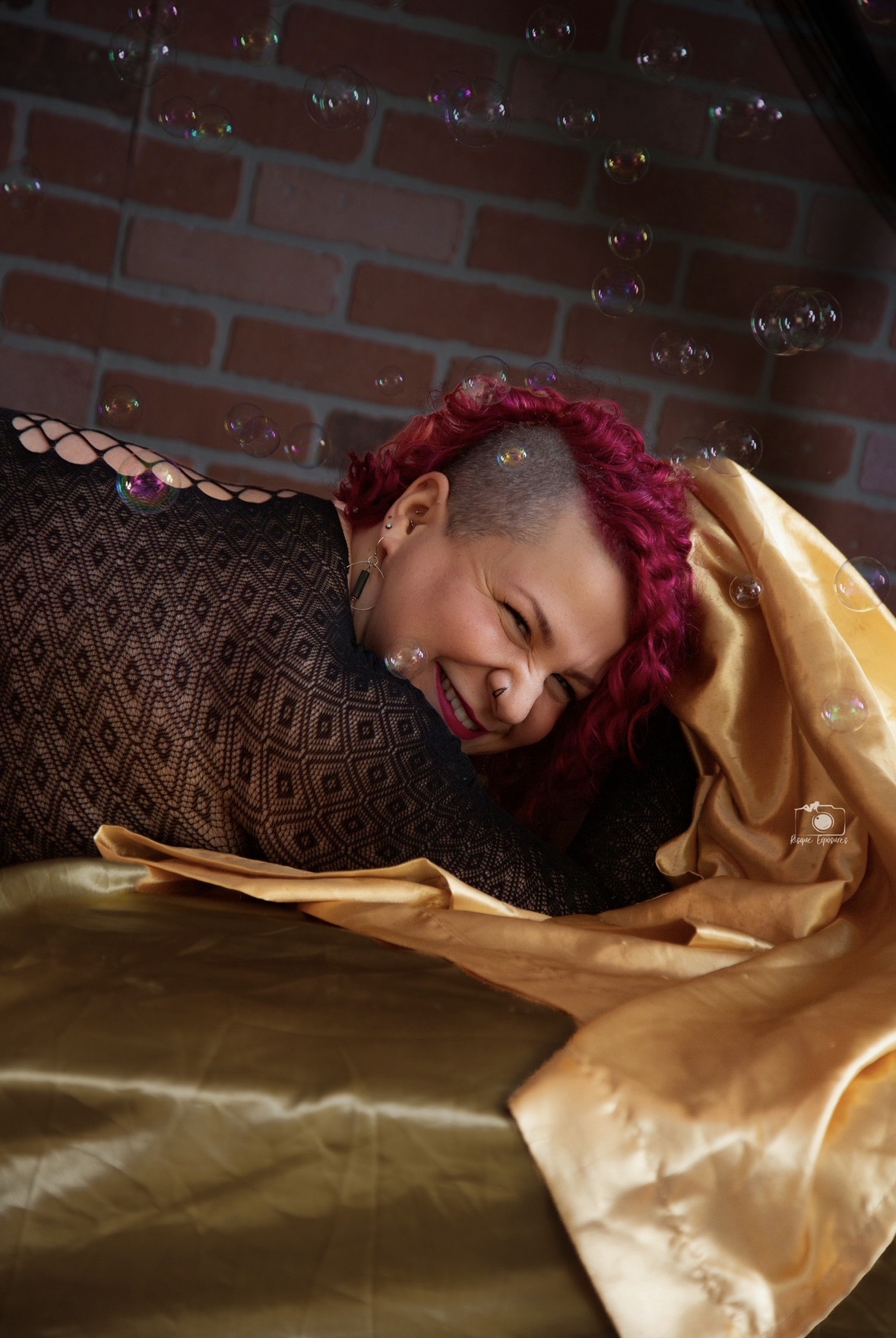 ember on a bed with gold sheets laughing with bubbles around her